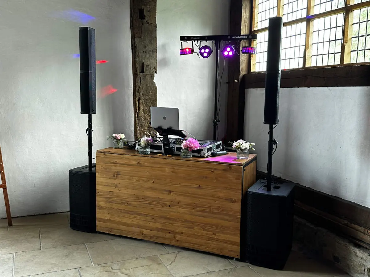 BASIC-Setup vor Ort: DJ-Pult in Holzoptik, Lautsprecher auf Stativen, Subwoofer und Lichtbar